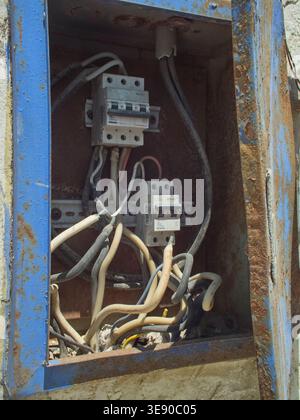 Colán, Piura, Perú, 27.03.2026, freiliegende elektrische Leitungen und Leistungsschalter in einem alten, korrodierten Anschlusskasten für den Außenbereich Stockfoto