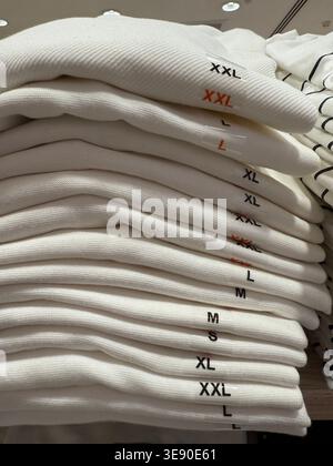 Gefaltete Pullover in verschiedenen Größen, ordentlich auf einem Regal gestapelt, geeignet als Hintergrund für den Einzelhandel. Mobiles Foto Stockfoto