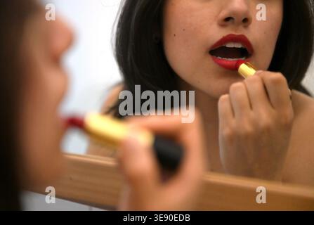 PRODUKTION - 10. Februar 2026, Berlin: Eine junge Frau trägt roten Lippenstift vor einem Spiegel auf. Foto: ELISA Schu/dpa Stockfoto