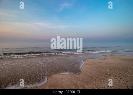 Ruhige Meereswellen, die auf den Sandstrand unter weichem Pastellhimmel strömen, Long Island, New York Stockfoto