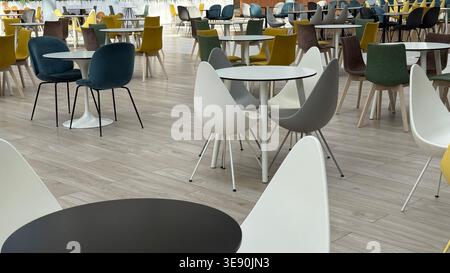 Moderne Cafeteria mit leeren Tischen und bunten Stühlen auf hellem Holzfußboden. Mobiles Foto Stockfoto