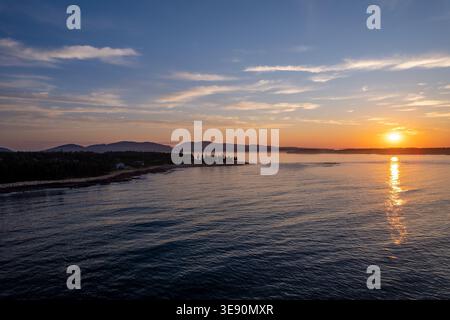 Goldener Sonnenuntergang über dem ruhigen Ozean mit weit entfernten, von Bäumen bedeckten Inseln und Bergen im Acadia-Nationalpark an der Küste von Maine. Stockfoto
