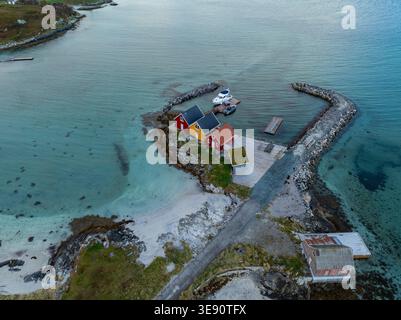 Blick aus der Vogelperspektive auf farbenfrohe Holzhäuser auf einer kleinen Halbinsel, umgeben von türkisfarbenem Wasser und einem Steinbruch in Sommaroy, Troms, Norwegen. Stockfoto