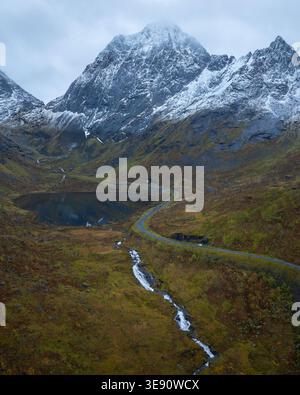 Aus der Vogelperspektive einer gewundenen Straße durch ein Tal mit einem kleinen See und einem Bach, der zu einem schneebedeckten Berggipfel in Senja, Troms, Norwegen führt. Stockfoto