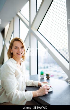 Frau lächelt, während sie Kaffee in einem modernen Café genießt Stockfoto