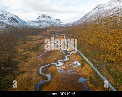 Aus der Vogelperspektive auf einen sich windenden Fluss und eine Straße durch ein Herbsttal mit schneebedeckten Bergen Senja, Troms, Norwegen. Stockfoto