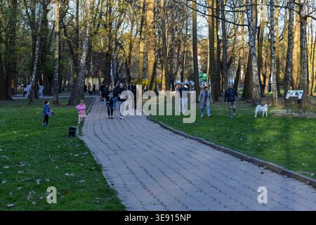 Menschen, die während eines sonnigen Frühlingabends in einem Stadtpark spazieren gehen und sich entspannen Stockfoto