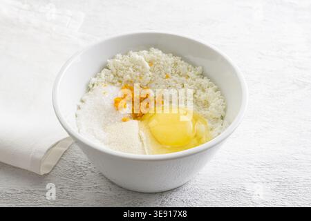 Zutaten für Ricotta-Käse in einer weißen Schüssel mit rohem Ei, Orangenschale und Zucker auf dem Küchentisch Stockfoto