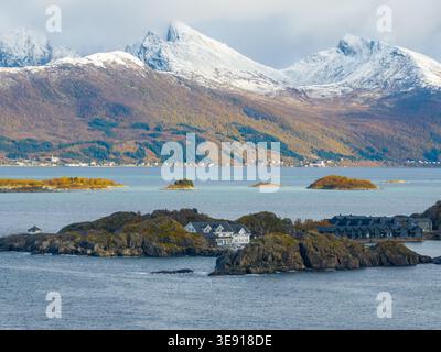 Blick aus der Vogelperspektive auf das Hamn i Senja Resort auf einer felsigen Insel, umgeben von türkisfarbenem Wasser und schneebedeckten Bergen in Skaland, Troms, Norwegen. Stockfoto