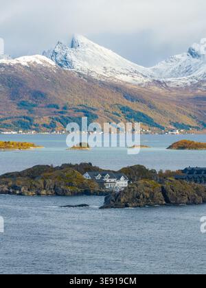 Blick aus der Vogelperspektive auf das Resort Hamn i Senja auf felsigen Inseln mit schneebedeckten Bergen und Herbstlaub in Skaland, Troms, Norwegen. Stockfoto
