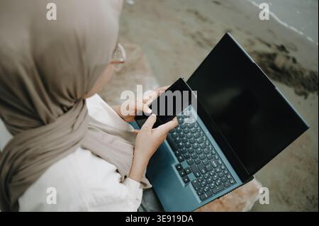 Muslimische Frau, die Remote mit einem Laptop arbeitet, auf Rocks in Nature, Outdoor Freelance Lifestyle, Digital Nomad, Unternehmensproduktivität in einer landschaftlich reizvollen Umgebung Stockfoto