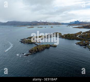 Blick aus der Vogelperspektive auf Hamn i Senja Resort und Hafen eingebettet zwischen felsigen Inseln und dunkelblauem Wasser mit schneebedeckten Bergen unter einem bewölkten Himmel Skaland, Stockfoto