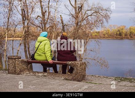 Zwei ältere Frauen entspannen auf einer Bank in der Nähe eines Sees. Stockfoto