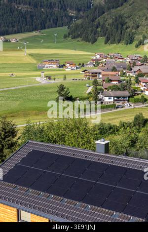 Solarpaneele bedecken Dach Landschaft Haus alpines Dorf grüne Felder, Waldberge helles Sonnenlicht. Erneuerbare Energieträger verbinden sich mit ländlichen Gebieten Stockfoto