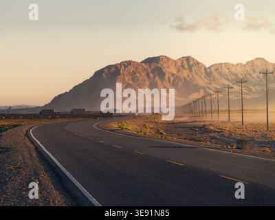 Eine kurvenreiche Straße führt zu sonnendurchfluteten Bergen durch eine staubige Landschaft Stockfoto