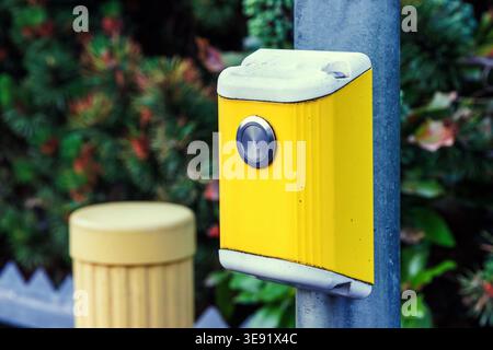 Nahaufnahme eines gelben Druckknopfes für Fußgänger, der an einem Stab befestigt ist. Städtische Straßeninfrastruktur Stockfoto