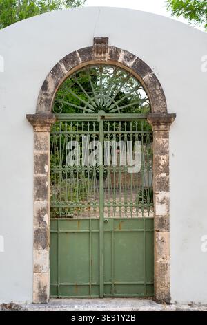 Grünes schmiedeeisernes Tor mit dekorativen Mustern in einem Steinbogen in einer weißen Putzwand, die verwitterte Textur zeigt. Stockfoto