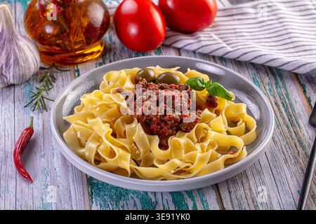 Ein Teller köstlicher italienischer Tagliatelle mit einer herzhaften Bolognese-Fleischsauce, garniert mit Basilikum und Oliven. Diese wohltuende Mahlzeit wird auf Rost serviert Stockfoto