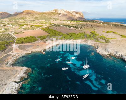 Aus der Vogelperspektive auf das türkisfarbene Wasser einer felsigen Bucht mit verankerten Segelbooten und Yachten entlang der zerklüfteten Küste und grünen Hügeln in Favignana, Sicili Stockfoto