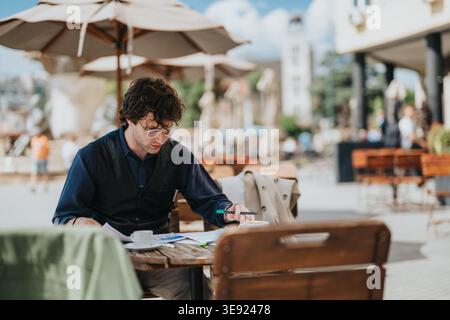 Mann, der an Dokumenten mit Kaffee arbeitet, an einem Café-Tisch im Freien auf einem Stadtplatz Stockfoto