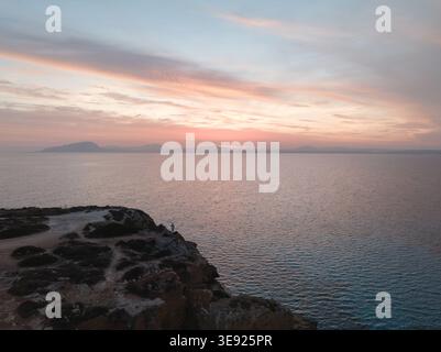 Blick aus der Vogelperspektive auf den Strand Bue Marino mit felsigen Klippen und einer Person, die bei einem sanften Sonnenuntergang über dem Mittelmeer auf Sizilien, Italien, am Rand steht. Stockfoto