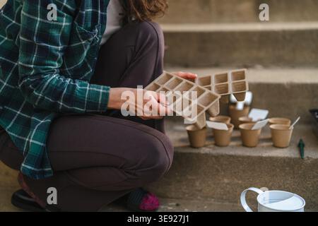 Frauenhände halten ein Tablett mit biologisch abbaubaren Torftöpfen, bereiten sich auf die Gartenarbeit vor und Pflanzen Samen auf umweltfreundliche Weise für nachhaltiges Grünzeug Stockfoto