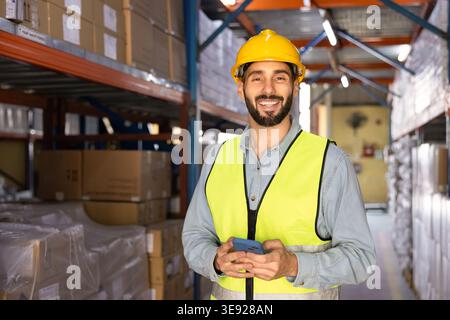 Porträt eines Arbeiters in Uniform, der das Smartphone im Lager hält Stockfoto