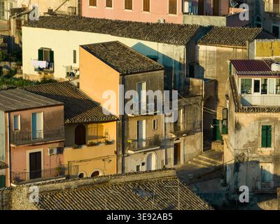 Blick aus der Vogelperspektive auf historische Steinhäuser mit traditionellen Ziegeldächern und Balkonen unter warmem, goldenem Licht in Ragusa, Sizilien, Italien. Stockfoto