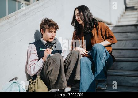 Zwei Schüler studieren gemeinsam auf Stufen im Freien und tauschen sich mit ihnen Notizen und Gesprächen aus Stockfoto