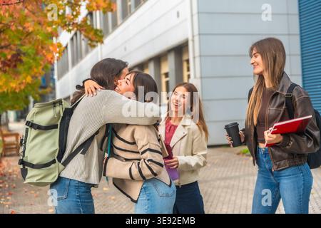 Junge Studentinnen, die sich auf dem Universitätscampus umarmen Stockfoto