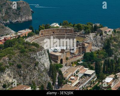 Blick aus der Vogelperspektive auf das antike Theater von Taormina mit seinem historischen Amphitheater aus Stein mit Blick auf das blaue Mittelmeer und die felsigen Klippen in Taormin Stockfoto