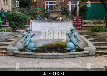 Der Viscount Southwood Gedenkbrunnen mit bronzenen Cherubfiguren auf einem ruhigen Londoner Gartenplatz, auf dem die Menschen auf Bänken ruhen Stockfoto