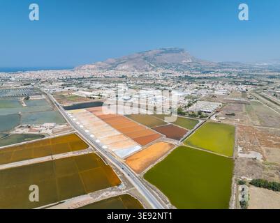 Aus der Vogelperspektive auf die farbenfrohen Salzdampfteiche und die Industrielandschaft unter einem klaren blauen Himmel in Marsala, Sizilien, Italien. Stockfoto
