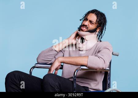 Arabischer Mann mit schmerzhaftem Gesichtsausdruck, der wegen Nackenverletzungen versorgt wird. Junge Patientin mit grimmiger Gesichter mit Halsband, die sich nach Unfall im Rollstuhl erholt Stockfoto