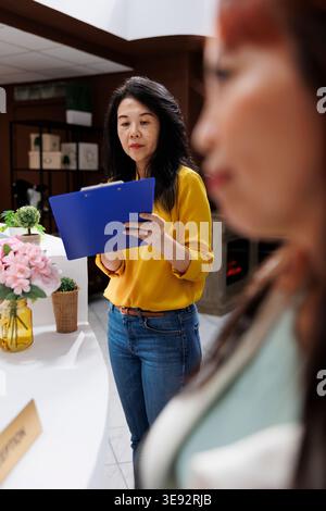 Neue Gäste sehen sich während ihrer Reise das Anmeldeformular an, um an der Rezeption in ein modernes Hotel einzuchecken. Asiatischer Reisender mittleren Alters bereitet sich darauf vor, in extravagantes Resort eingecheckt zu werden Stockfoto