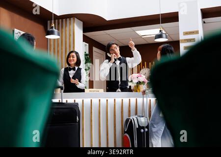 Der junge asiatische Rezeptionist weist den ankommenden Touristen auf das Zimmer in der Lobby des extravaganten Resorts. Professioneller männlicher Concierge, der Neukunden zur Unterkunft an der Rezeption des gemütlichen Hotels führt Stockfoto