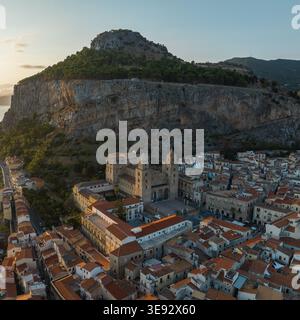 Aus der Vogelperspektive auf die historische Kathedrale von Cefalu und die rot gekachelten Dächer am Fuße der massiven Klippe La Rocca während der goldenen Stunde in Cefalu, Sizilien, IT Stockfoto