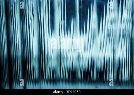 Vertikale abstrakte Lichtreflexionen in Cyan durch verzerrte, wellenförmige Glasstruktur Stockfoto