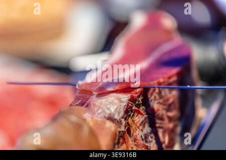 Fachkundige Hand, die dünne Stücke von Schinken schneiden. Eine Nahaufnahme des ausgehärteten Schinkens, der für den Verzehr zubereitet wird Stockfoto