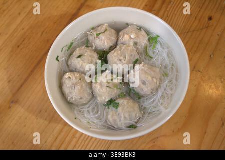 Eine Schüssel mit Fleischbällchen mit Reisvermicelli und Gemüse auf einem Holztisch Stockfoto