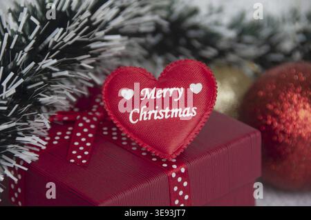 Frohe Weihnachten Text auf Herzform auf roter Farbe Geschenk mit Weihnachtsdekoration Hintergrund. Weihnachtsgeschenk- und Festkonzept Stockfoto