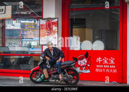 Senior Mann sitzt auf einem Motorrad vor einer Fassade des Roten Restaurants Stockfoto