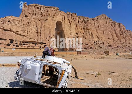 Junger Mann, der auf einem zerstörten russischen Panzer vor der Salsal-Buddha-Nische sitzt, Bamiyan-Tal, Afghanistan. Kriegsreste an der UNESCO-Stätte Stockfoto