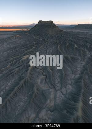Blick aus der Vogelperspektive auf Factory Butte und die umliegenden erodierten Badlands mit tiefen Graten unter einem sanften Sonnenuntergang im Wayne County, Utah, USA. Stockfoto