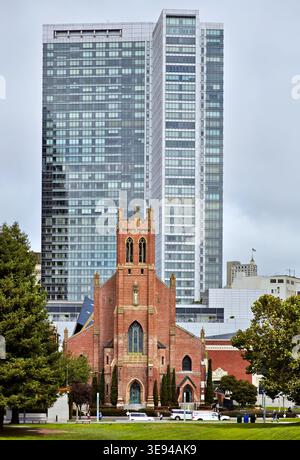 Die St. Patrick Church steht vor hohen Gebäuden in San Francisco. An einem bewölkten Tag spazieren die Menschen durch den Yerba Buena Park. Stockfoto