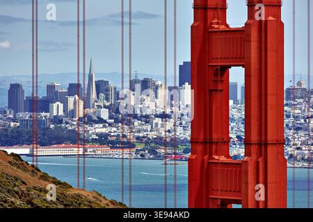 Die Skyline von San Francisco ist von der Golden Gate Bridge aus zu sehen. Wasser und Land mischen sich unter der Brückenkonstruktion an einem sonnigen Tag. Stockfoto