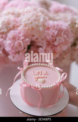 Kleiner rosafarbener bento-Kuchen, dekoriert mit Speiseperlen und Bändern für ein einjähriges Mädchen. Minimalistischer Kuchen mit weißem Herz und Schriftzug auf Paste Stockfoto
