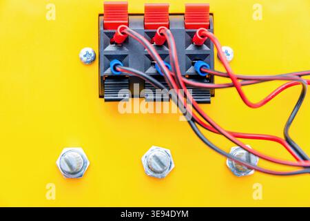 Nahaufnahme von roten und schwarzen Kabeln, die mit einem elektrischen Klemmenblock auf hellgelbem Hintergrund verbunden sind. Ideal für Audio-, Energie- und Stromkonzepte Stockfoto