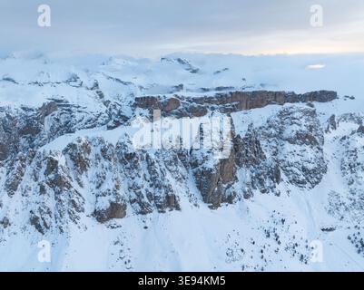 Aus der Vogelperspektive auf die schneebedeckten Gipfel und zerklüfteten Felsformationen der Dolomiten unter weichem Winterhimmel in Wolkenstein in Gröden, Trentino-Südtirol Stockfoto