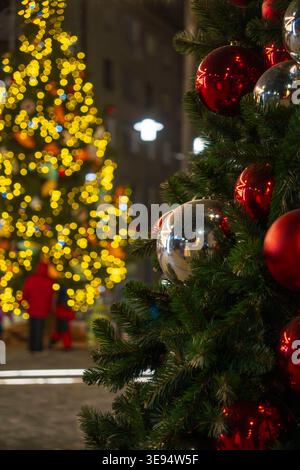 Im Vordergrund steht ein wunderschön dekorierter Weihnachtsbaum mit roten und silbernen Ornamenten, beleuchtet von warmen festlichen Lichtern. Im Hintergrund Stockfoto